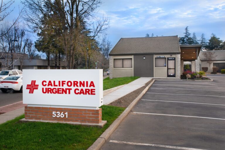 A white sign with red text reads California Urgent Care and stands in front of a small medical clinic building with an empty parking lot and trees in the background. The address 5361 is visible on the sign. | California Urgent Care Center