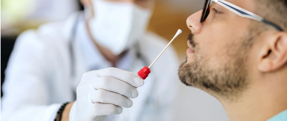 A healthcare professional wearing a mask and gloves holds a swab near a mans nose, preparing to collect a nasal sample for a medical test. | California Urgent Care Center